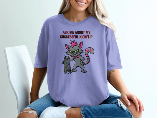Lavender t-shirt with a cartoon cat and text "Ask me about my successful kickflip".