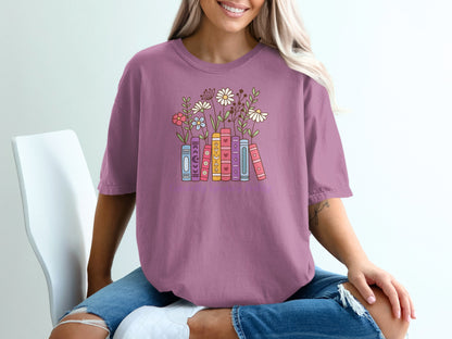 Purple t-shirt with colorful stacked books and flowers illustration.