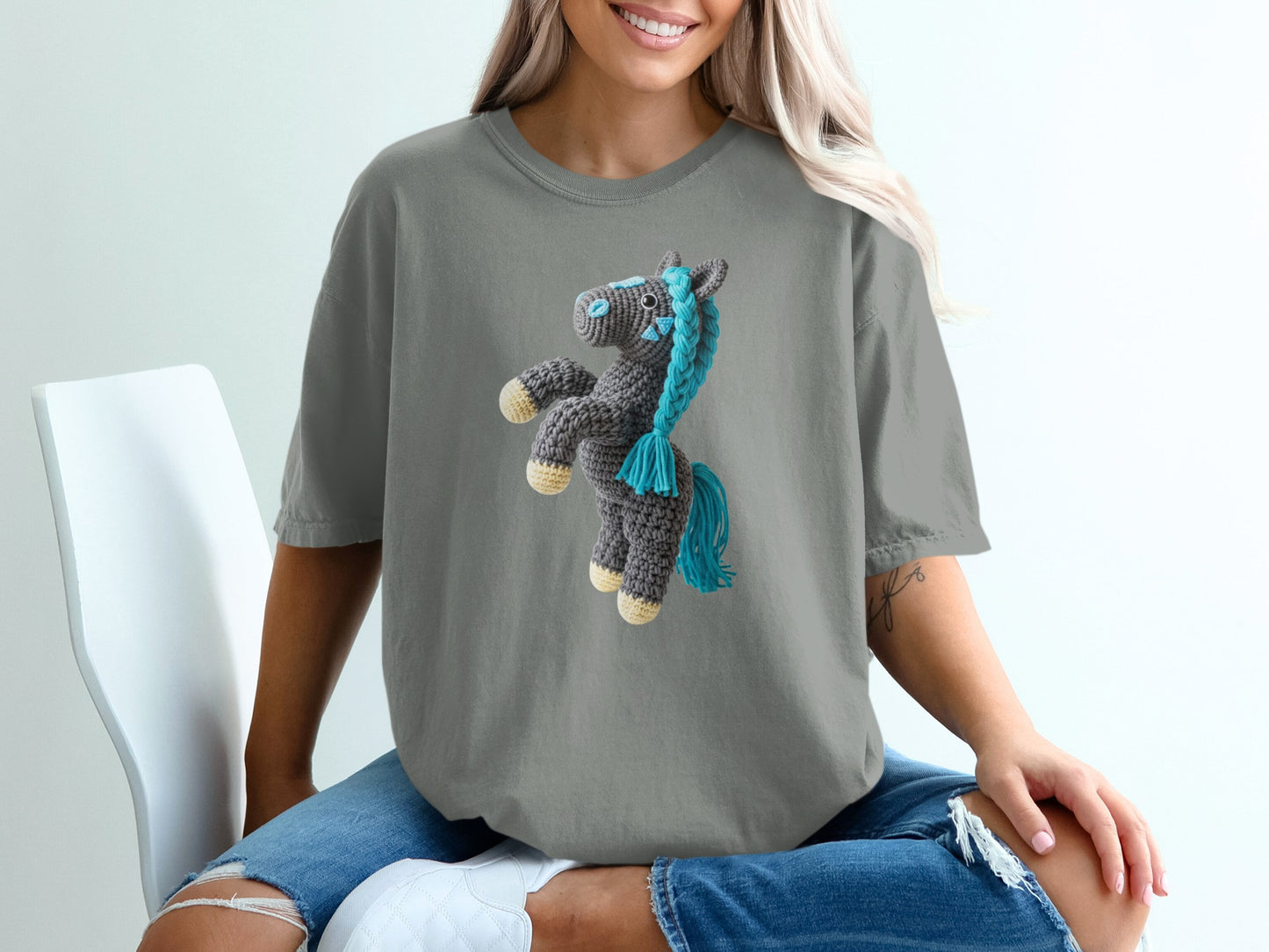 Crocheted grey horse with blue mane and tail on a grey t-shirt.