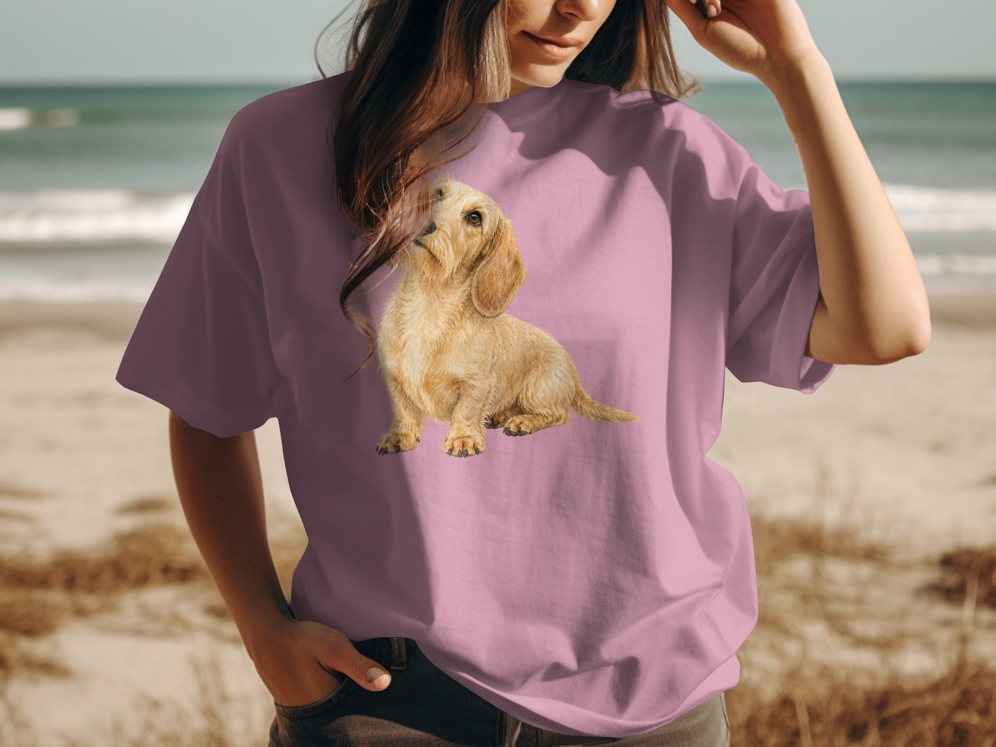 Pink t-shirt with a tan wire-haired dachshund graphic on a beach background.