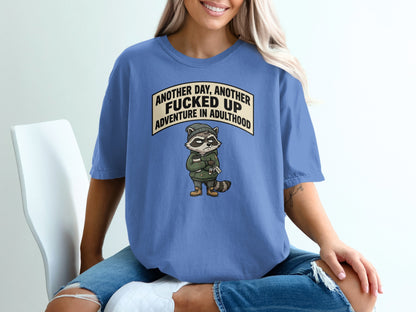 Raccoon wearing hoodie and beanie, holding coffee cup, text says "Another day, another fucked up adventure in adulthood".