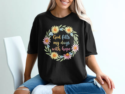 Black t-shirt with floral wreath and "God fills my days with hope" text.