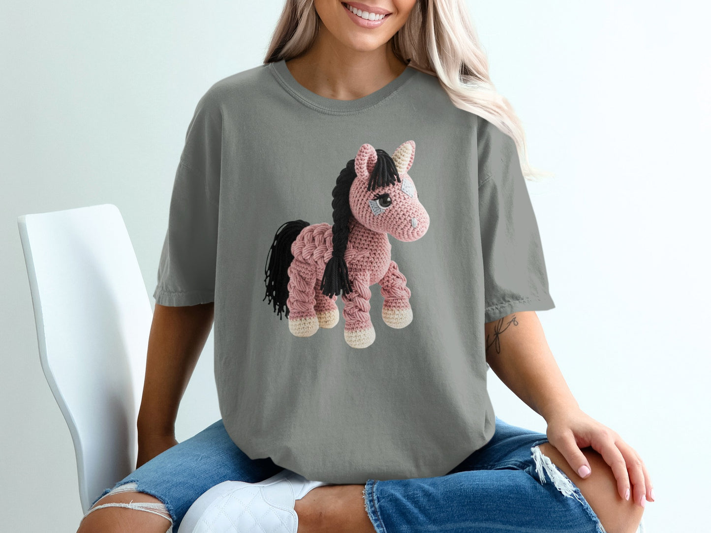 Crocheted pink horse with black mane on a grey t-shirt.