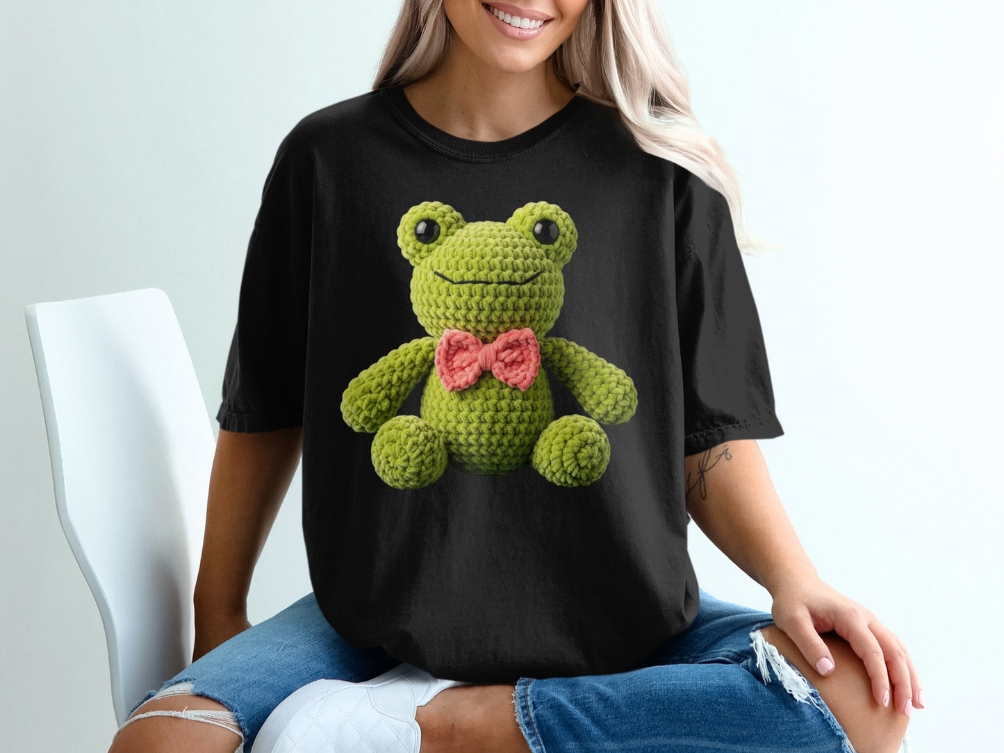 Crocheted green frog with pink bow on black t-shirt.