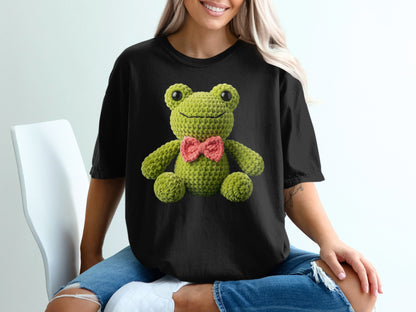 Crocheted green frog with pink bow on black t-shirt.
