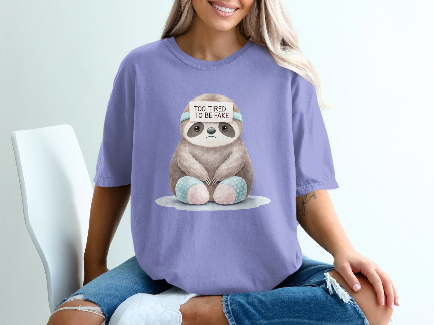 Sloth wearing a headband that says "TOO TIRED TO BE FAKE" on a t-shirt.