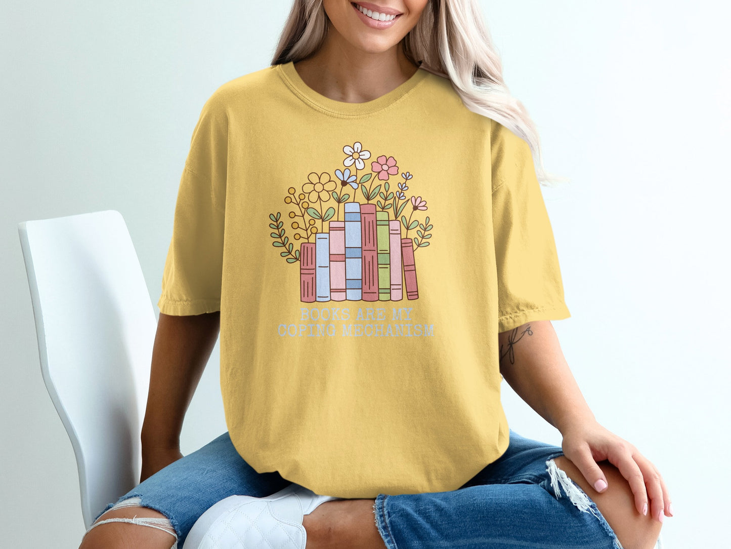 Yellow t-shirt with a stack of books and flowers, text "BOOKS ARE MY COPING MECHANISM".