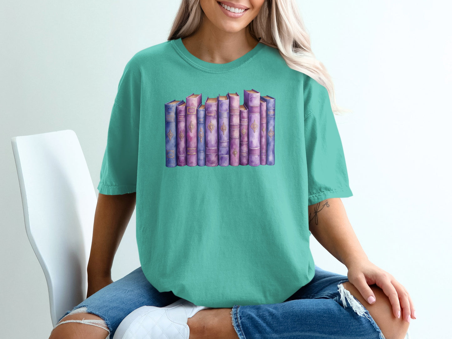 Watercolor books in purple and gold spines on a teal t-shirt.
