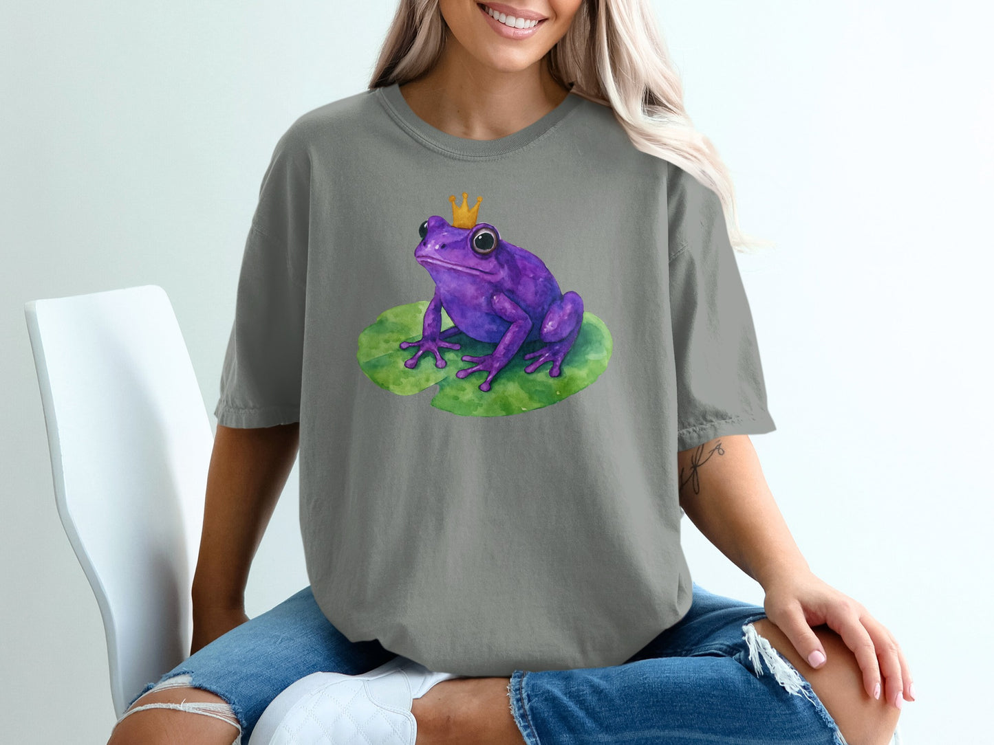 Purple frog with crown sits on a lily pad, graphic print on a gray t-shirt.