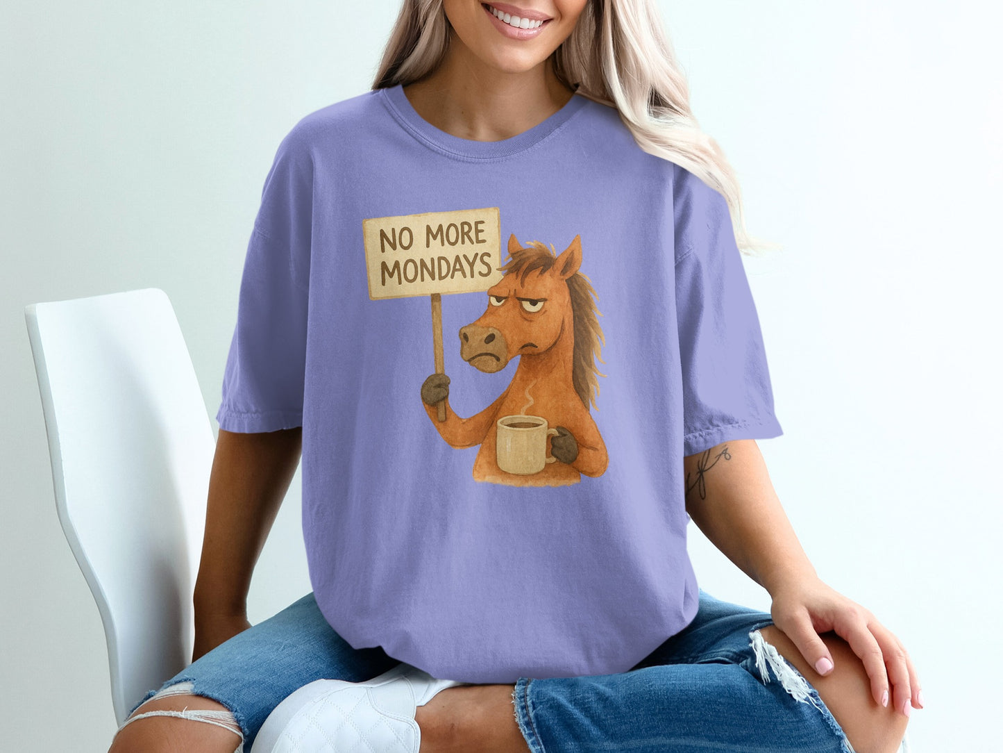 Horse holding "No More Mondays" sign and coffee mug, wearing a purple t-shirt.
