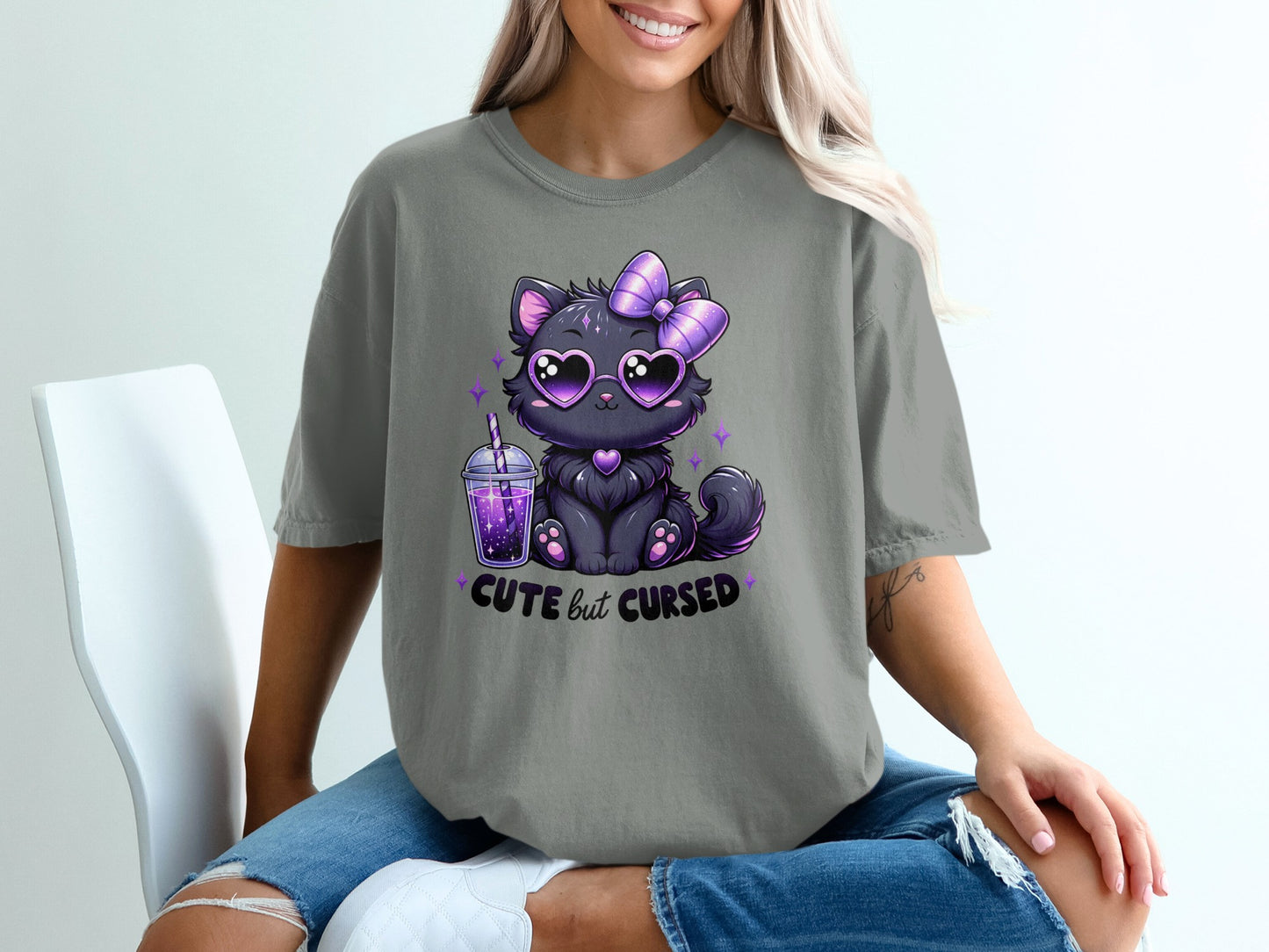 Black cat with heart sunglasses and purple bow on t-shirt saying "cute but cursed".
