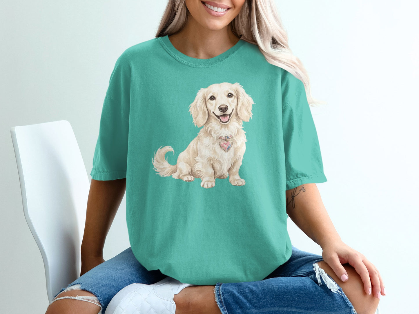 Cream dachshund wearing pink heart collar on teal t-shirt.