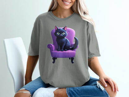 Black cat with green eyes sitting on a purple chair, wearing a gray t-shirt.