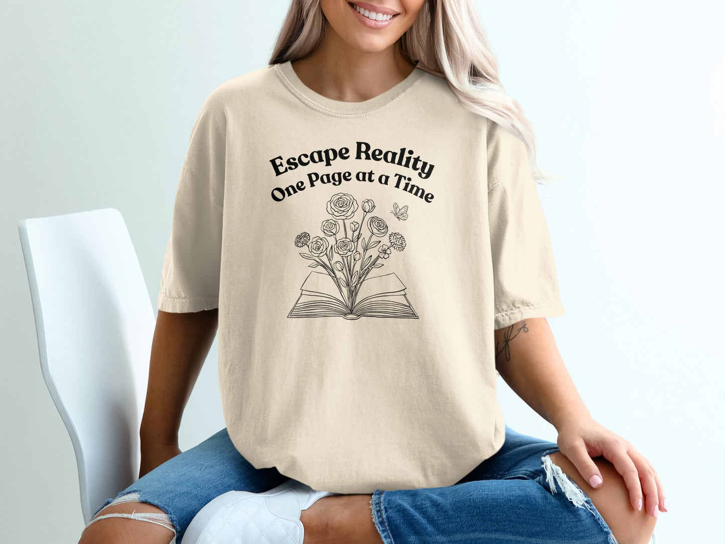 Cream t-shirt with "Escape Reality One Page at a Time" and an open book with flowers.
