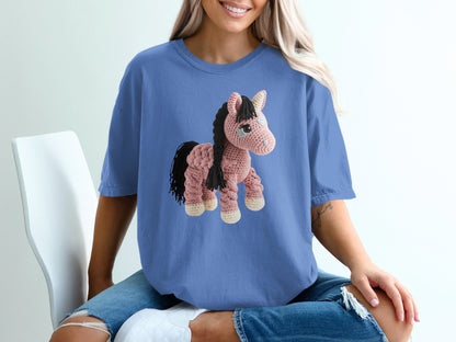 Crocheted pink horse with black mane and tail on a blue t-shirt.