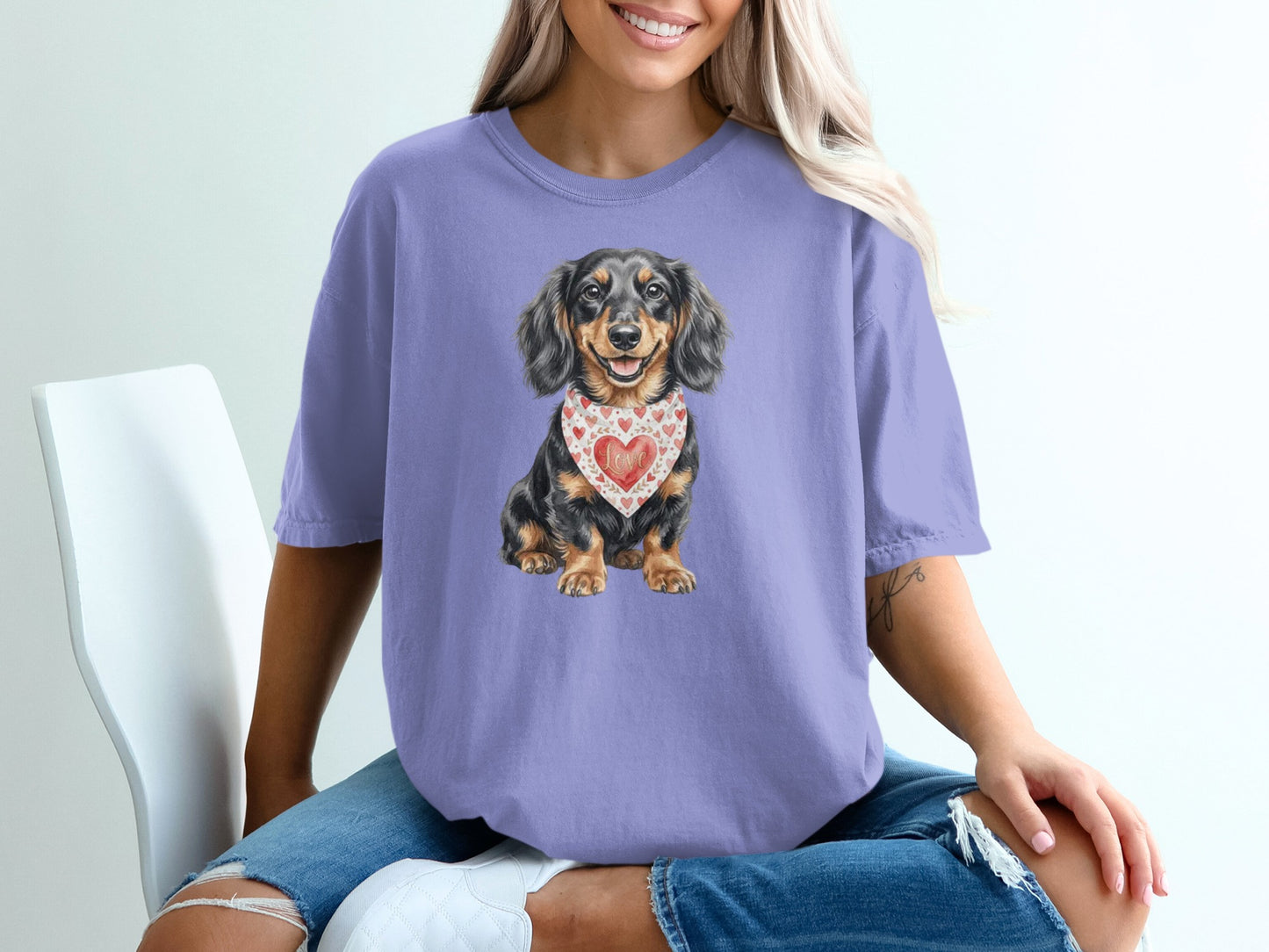 Dachshund dog wearing a heart-patterned bandana on a purple t-shirt.