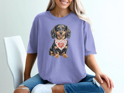 Dachshund dog wearing a heart-patterned bandana on a purple t-shirt.