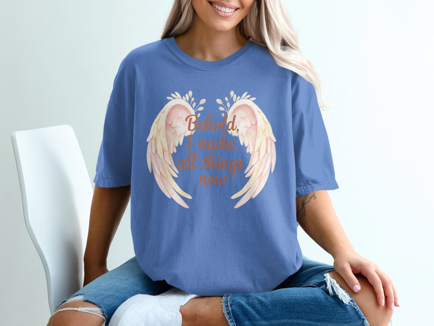 Blue t-shirt with cream feathered wings and text "Behold, I make all things new."