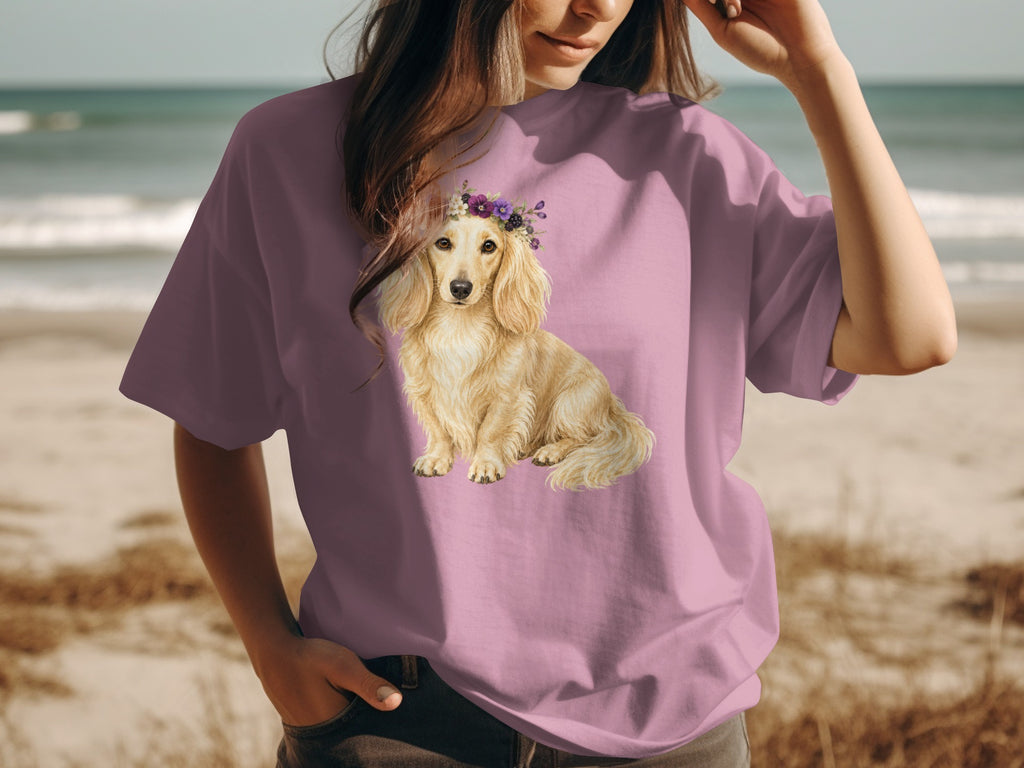 T-shirt with a light blonde dachshund wearing a floral crown on a beach.
