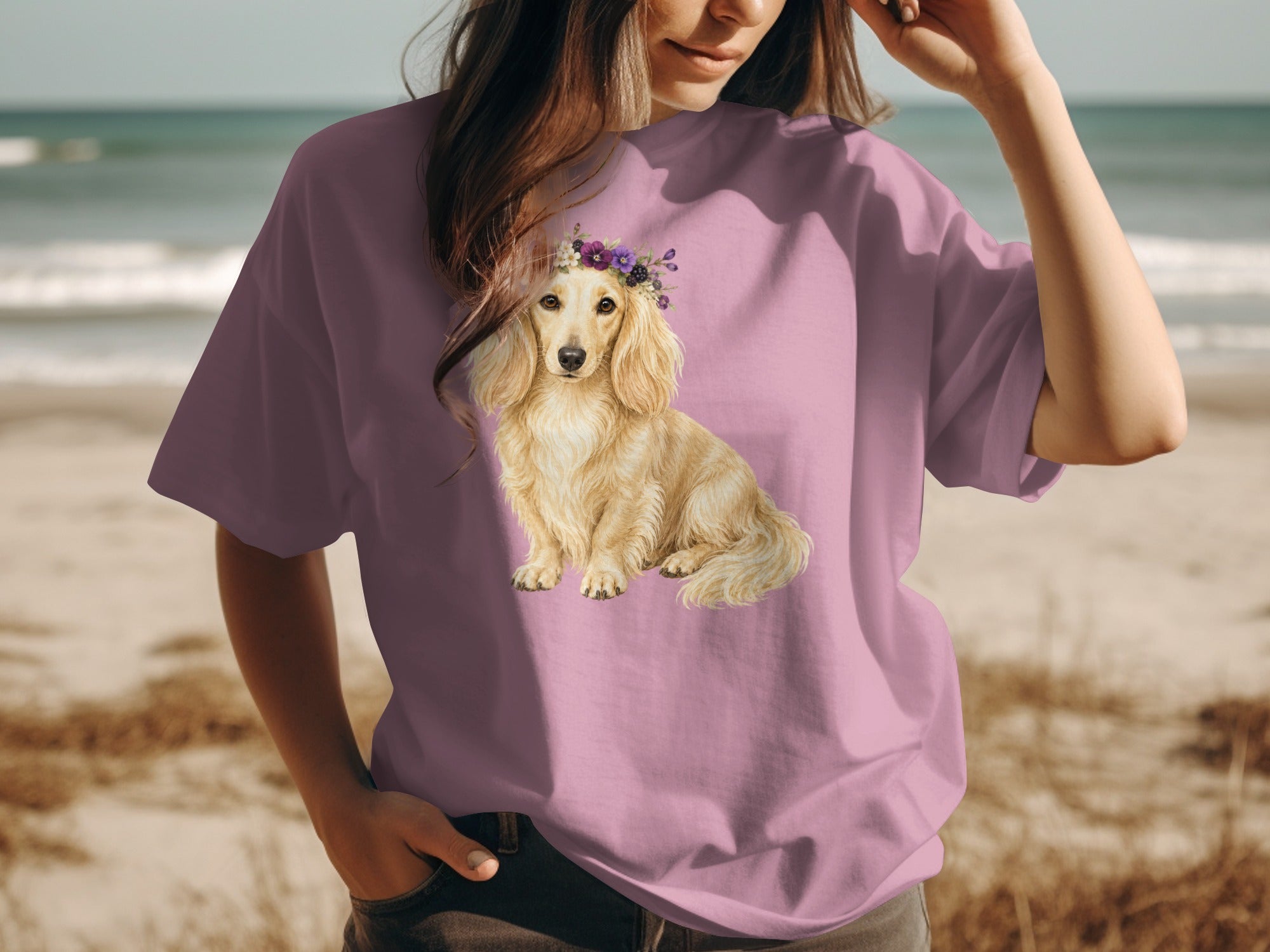 T-shirt with a light blonde dachshund wearing a floral crown on a beach.