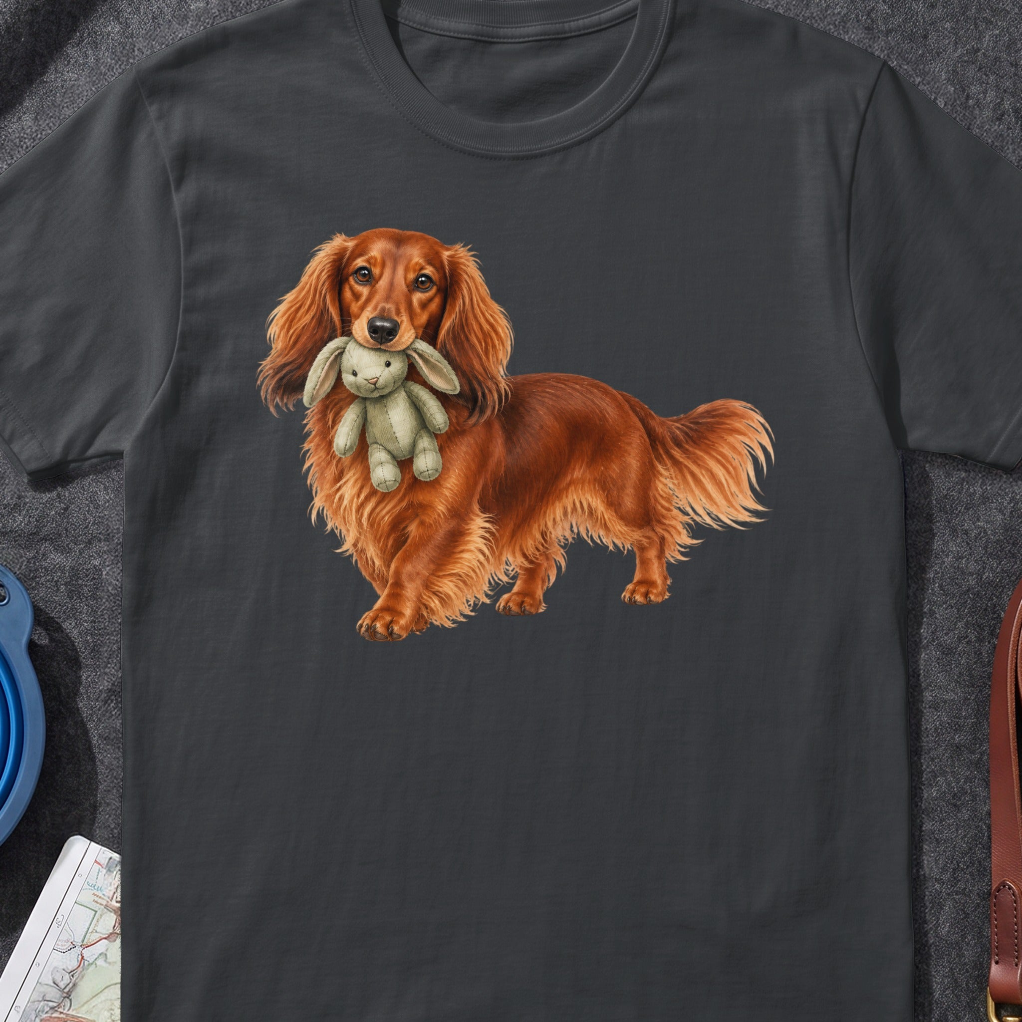 Long-haired dachshund holding a stuffed bunny in its mouth on a dark t-shirt.
