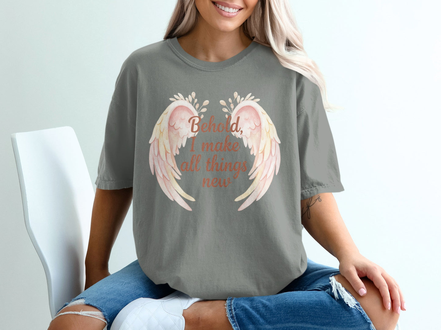 Grey t-shirt with pink wings and text "Behold, I make all things new".