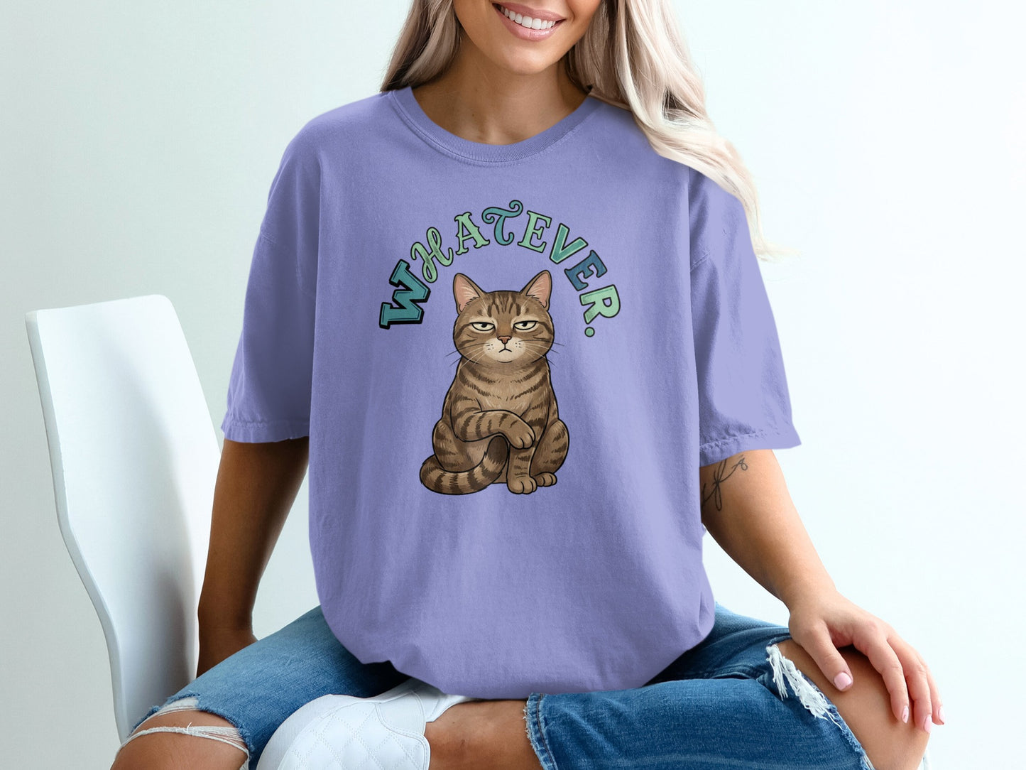 Cat wearing a t-shirt with "Whatever" text, sitting on a chair.