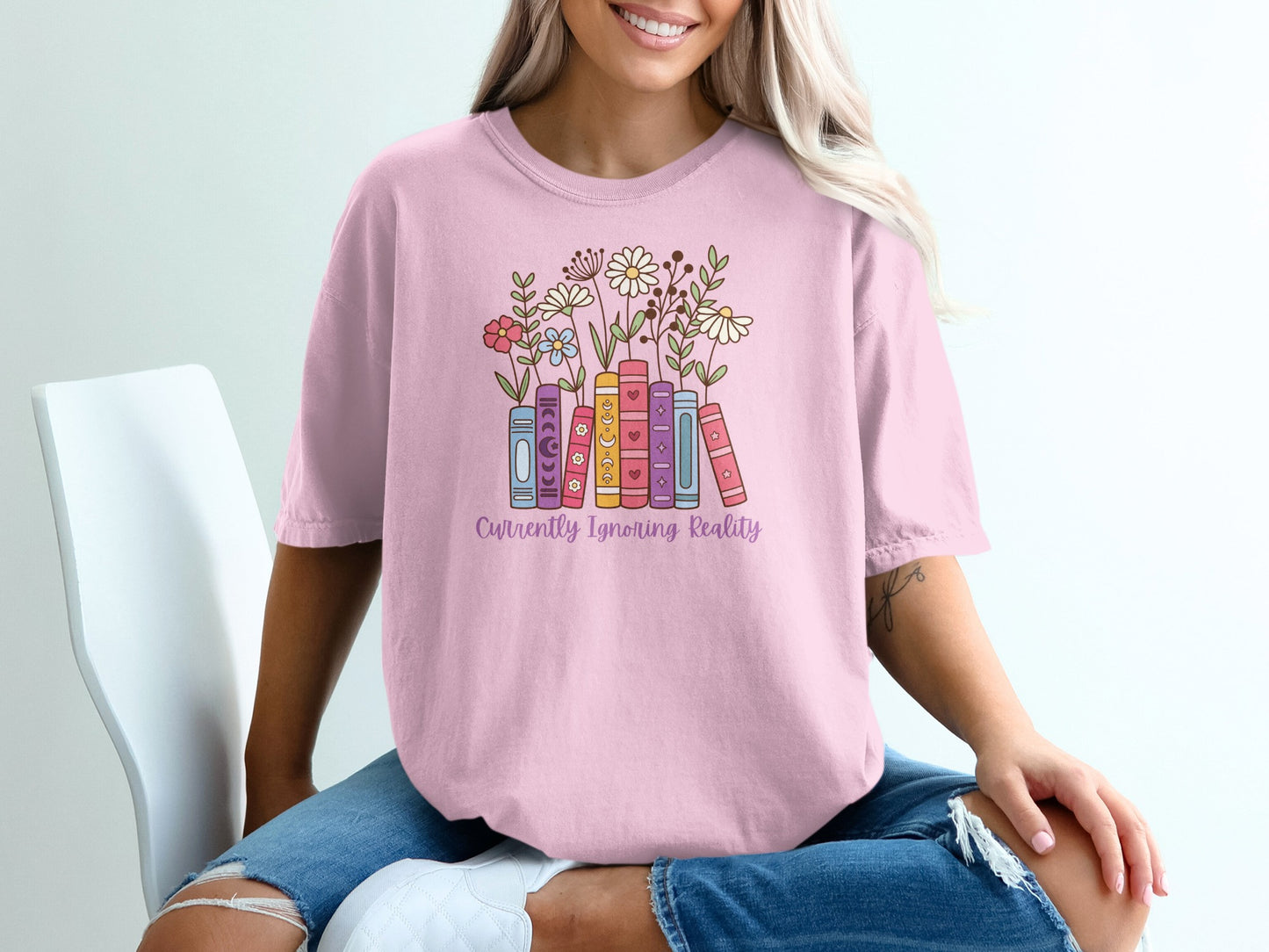 Pink t-shirt with stacked books and flowers, reading "Currently Ignoring Reality".