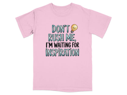 Pink t-shirt with "DON'T RUSH ME, I'M WAITING FOR INSPIRATION" text and lightbulb.