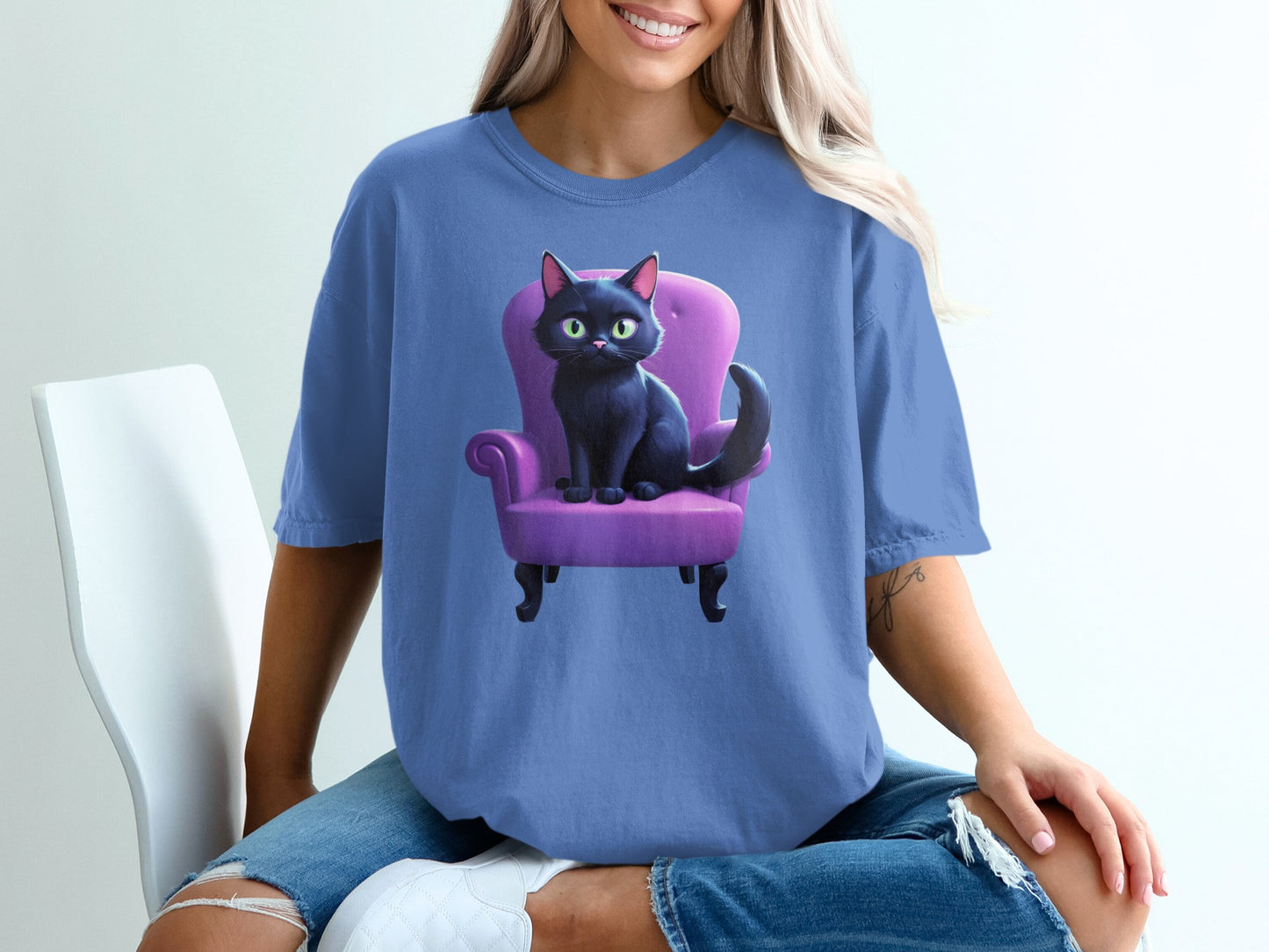 Black cat with green eyes sitting in a purple armchair on a t-shirt.