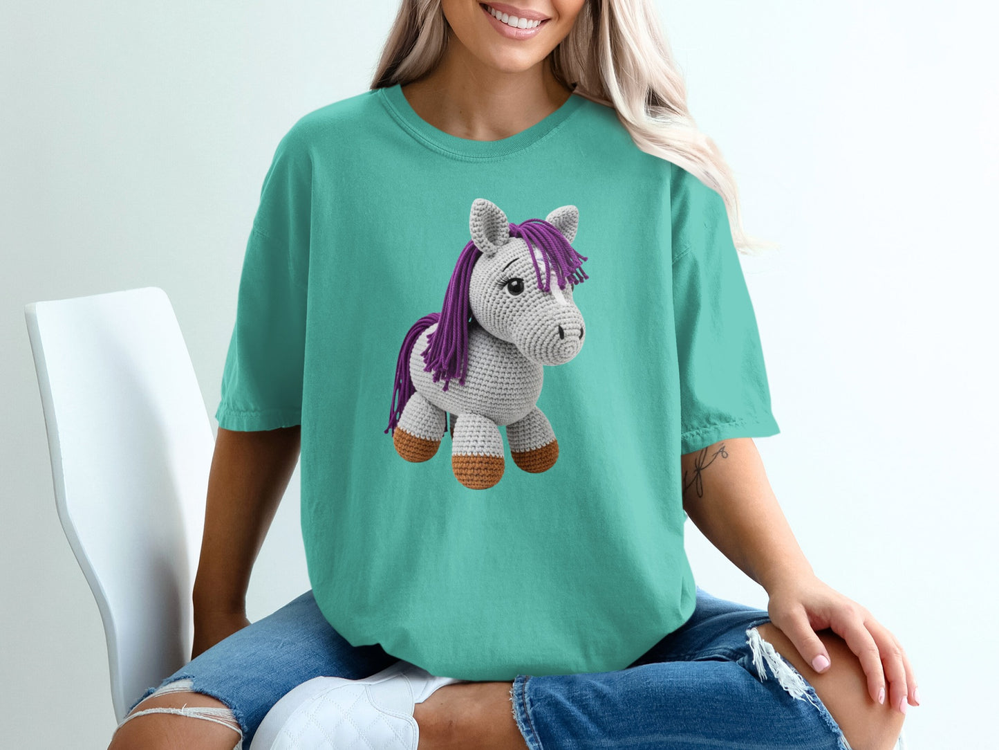 Teal t-shirt with a purple and white crocheted unicorn graphic.