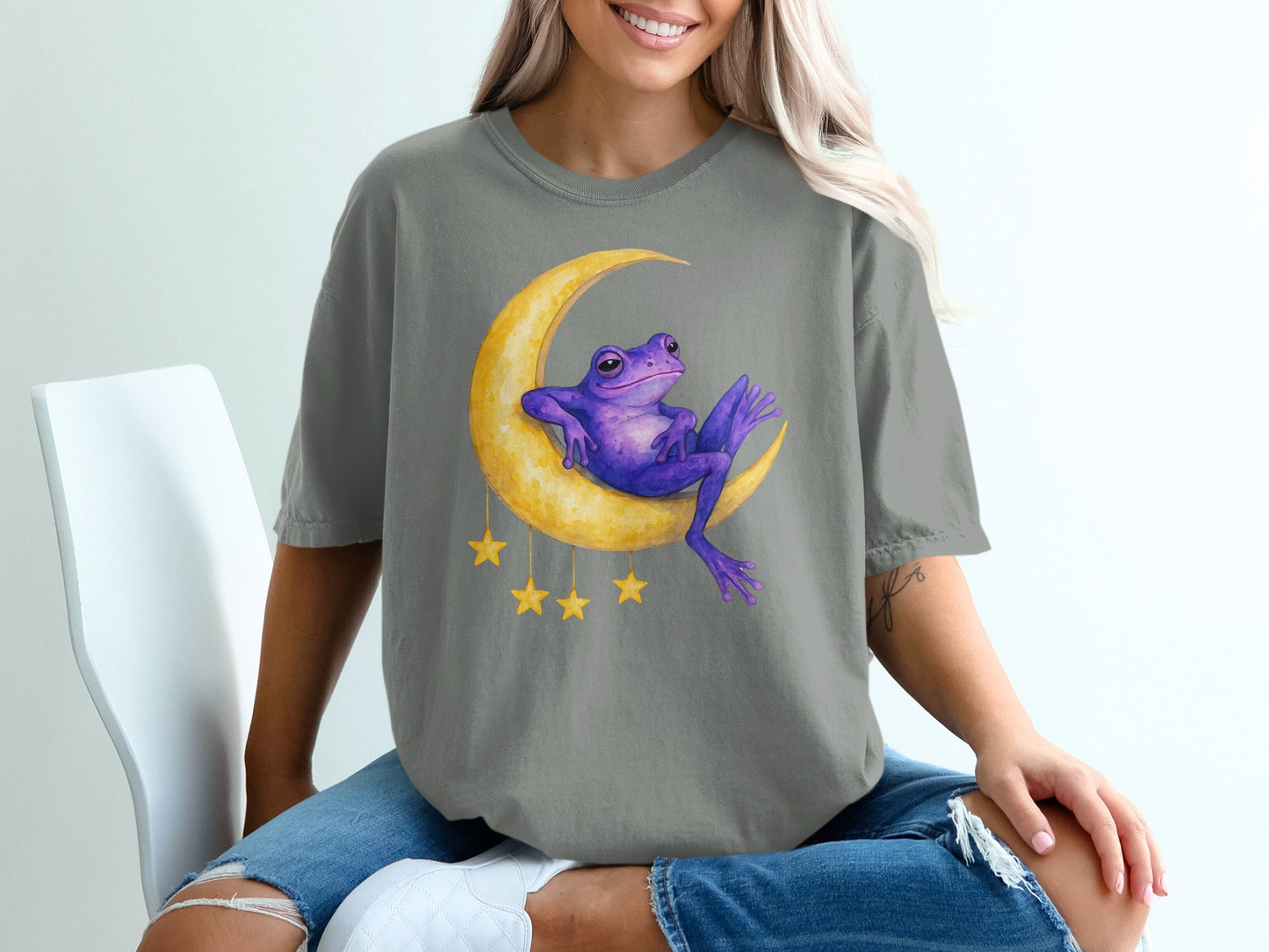 Purple frog sits on crescent moon with yellow stars.
