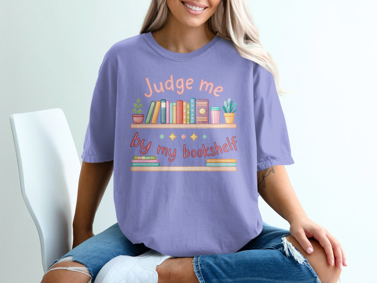Purple t-shirt with "Judge me by my bookshelf" and illustrated books.