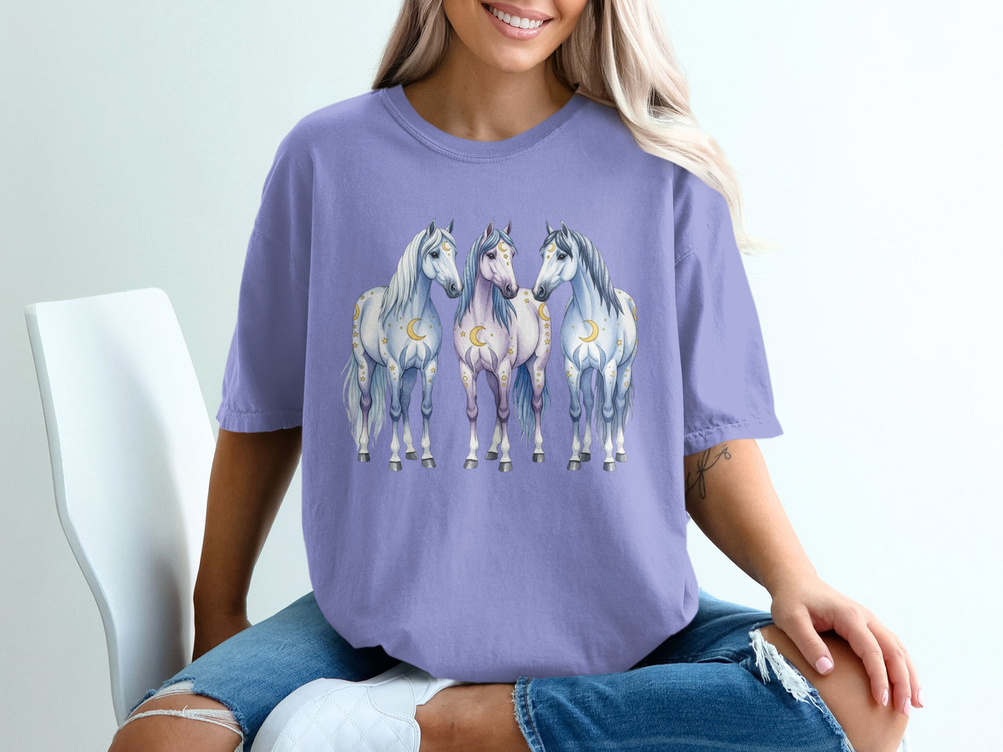 Three stylized horses with celestial accents on a purple t-shirt.