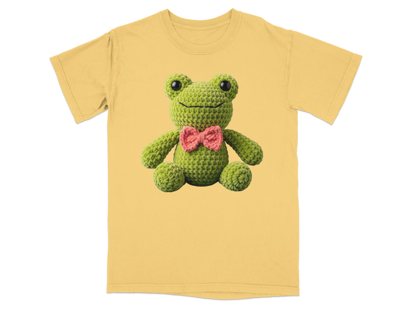 Green crochet frog with pink bow tie on a yellow t-shirt.