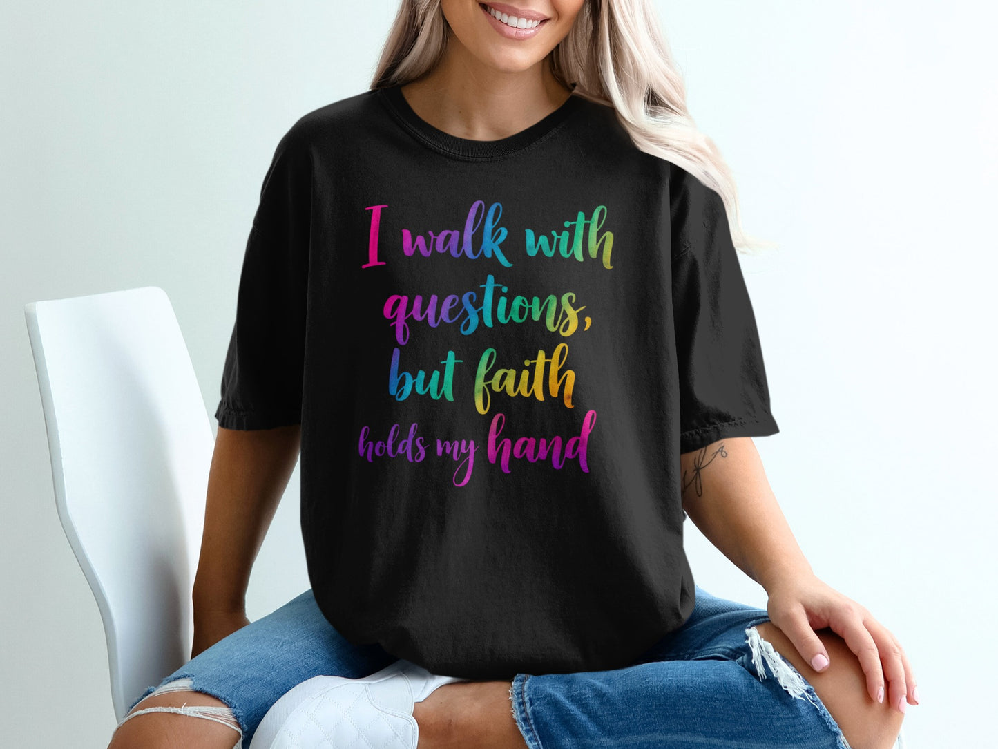 Black t-shirt with rainbow text reading "I walk with questions, but faith holds my hand".