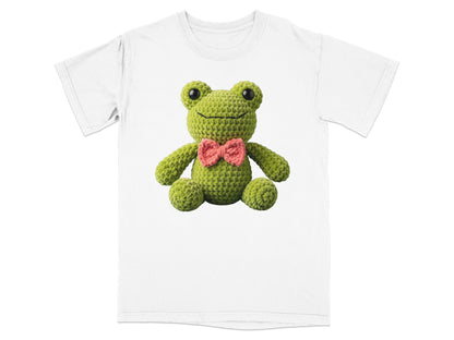 Green crocheted frog with pink bow tie on a white t-shirt.