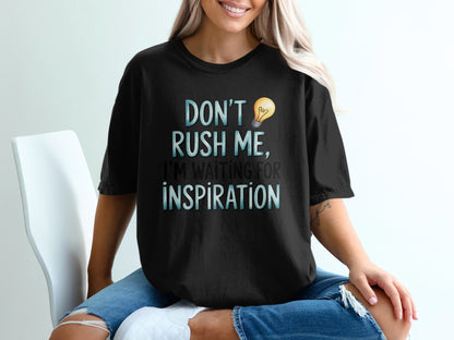 Black t-shirt with "DON'T RUSH ME, I'M WAITING FOR INSPIRATION" text and lightbulb.