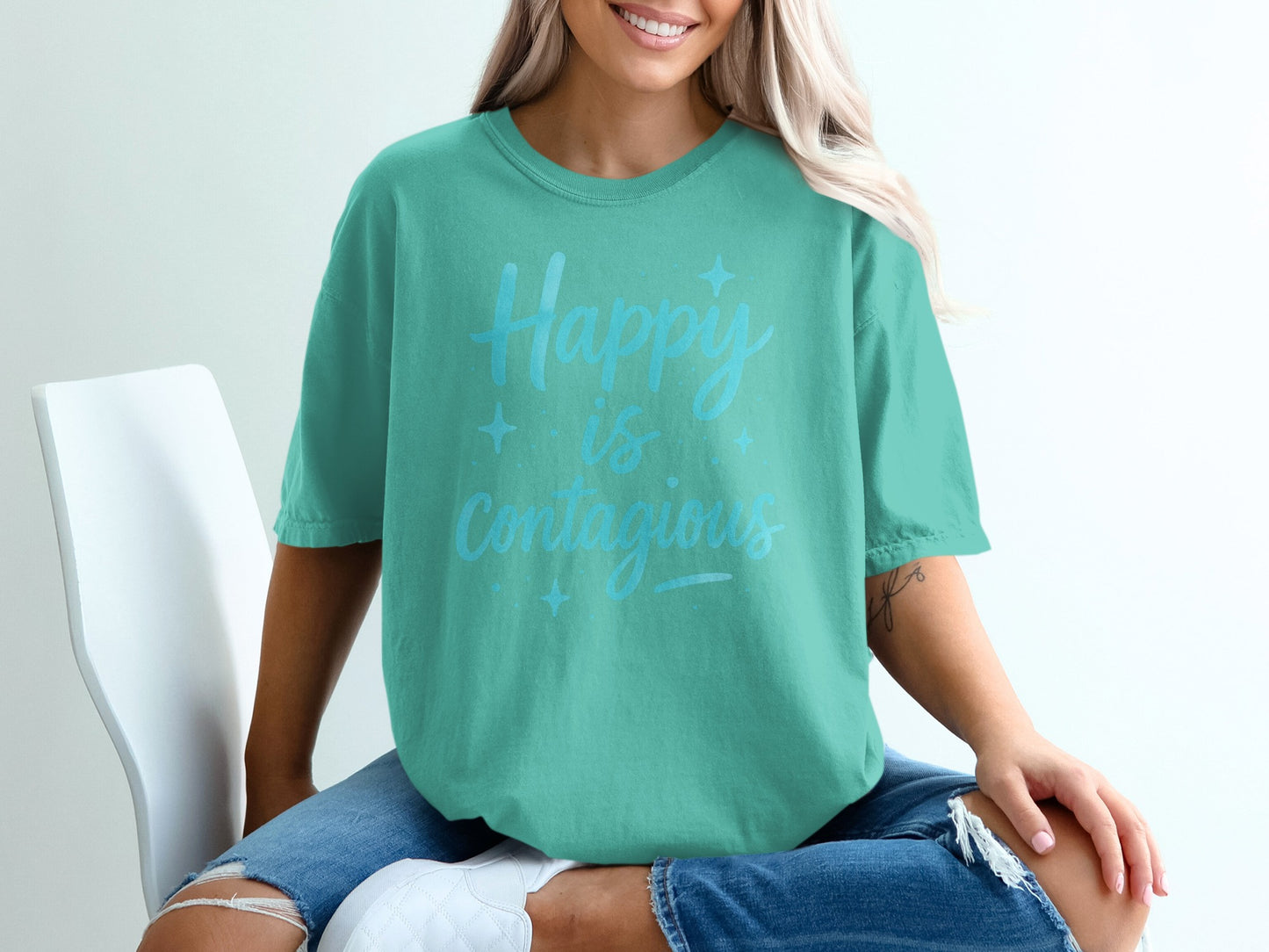 Teal t-shirt with "Happy is Contagious" text, worn by a woman.