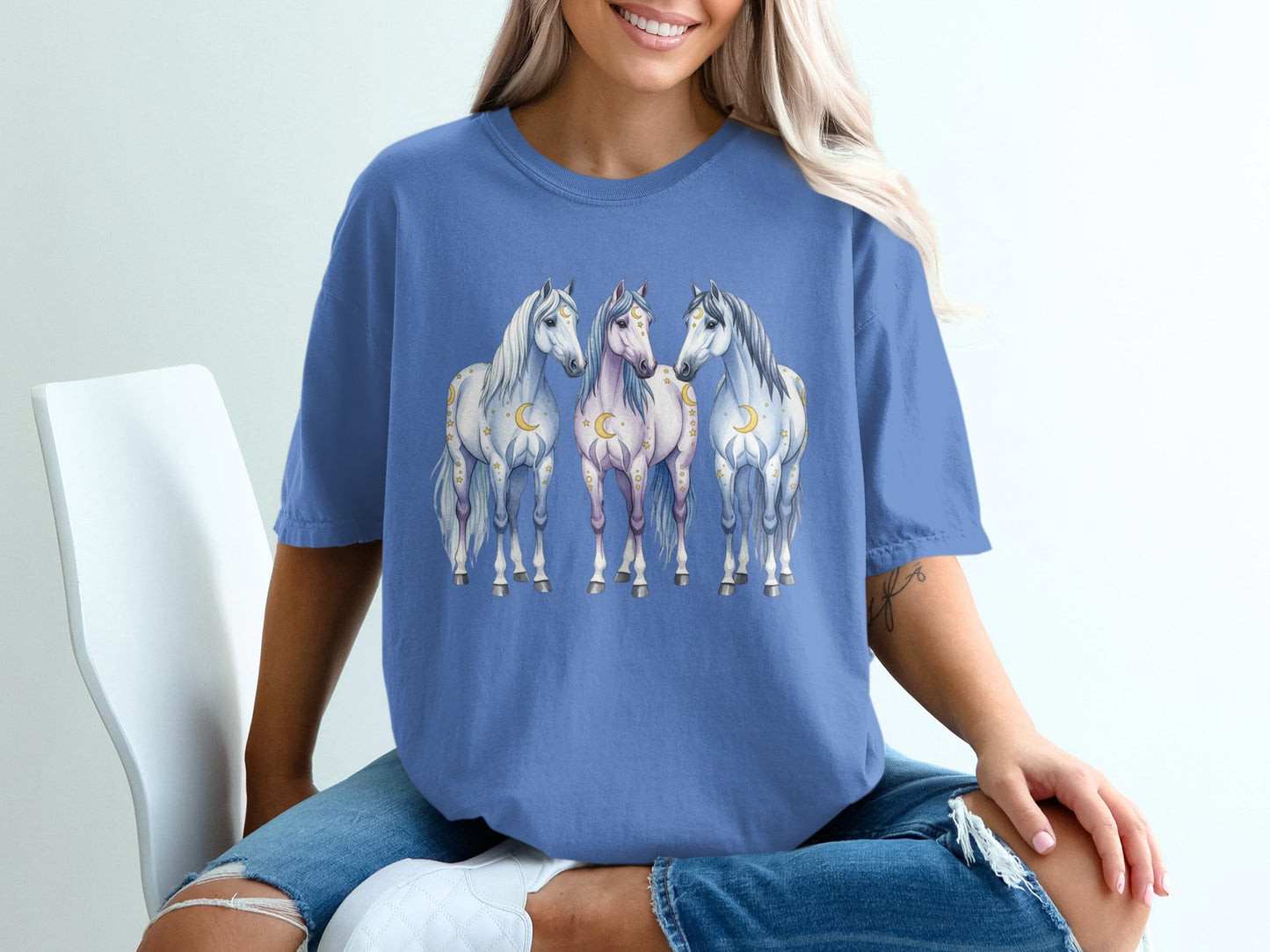 Three stylized horses with celestial accents on a blue t-shirt.