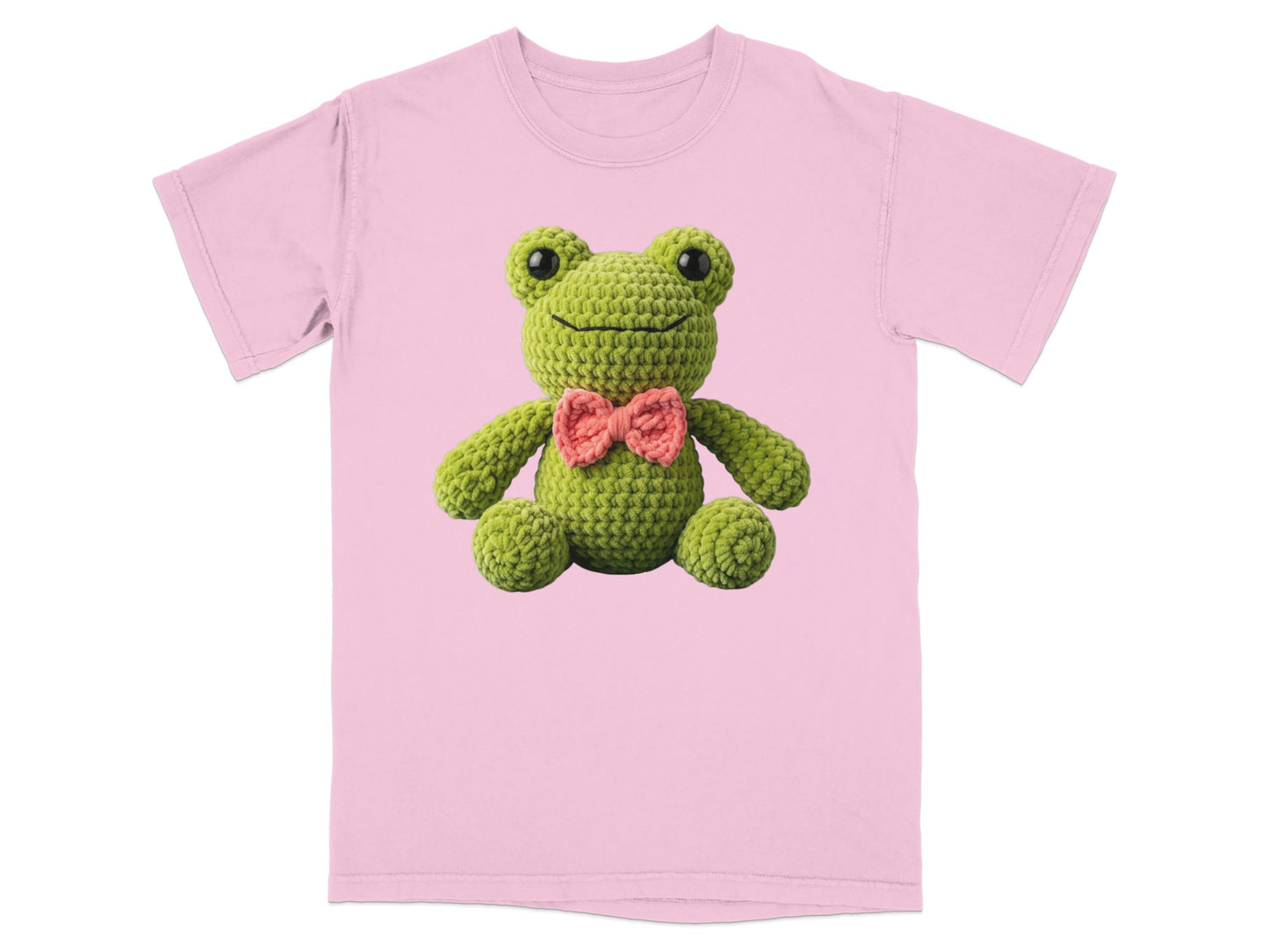 Crocheted green frog wearing a pink bow tie on a pink t-shirt.