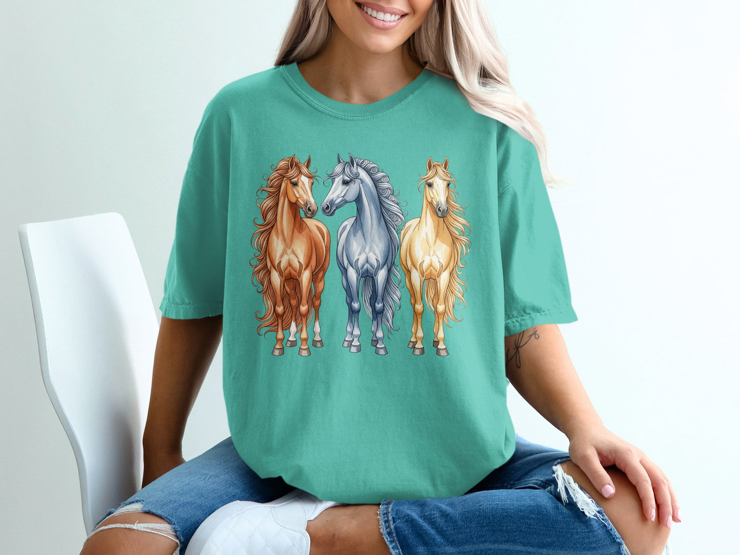 Three watercolor horses in white, brown, and tan on a teal t-shirt.