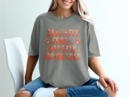 Grey t-shirt with orange text "Slightly feral, mostly adorable" and paw prints.