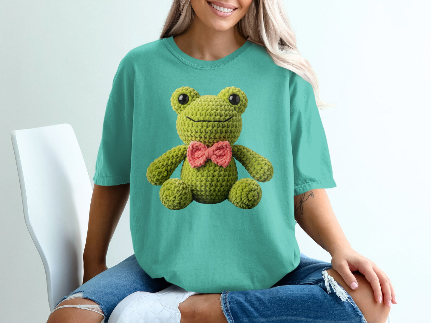 Teal t-shirt with a knitted green frog wearing a pink bow.