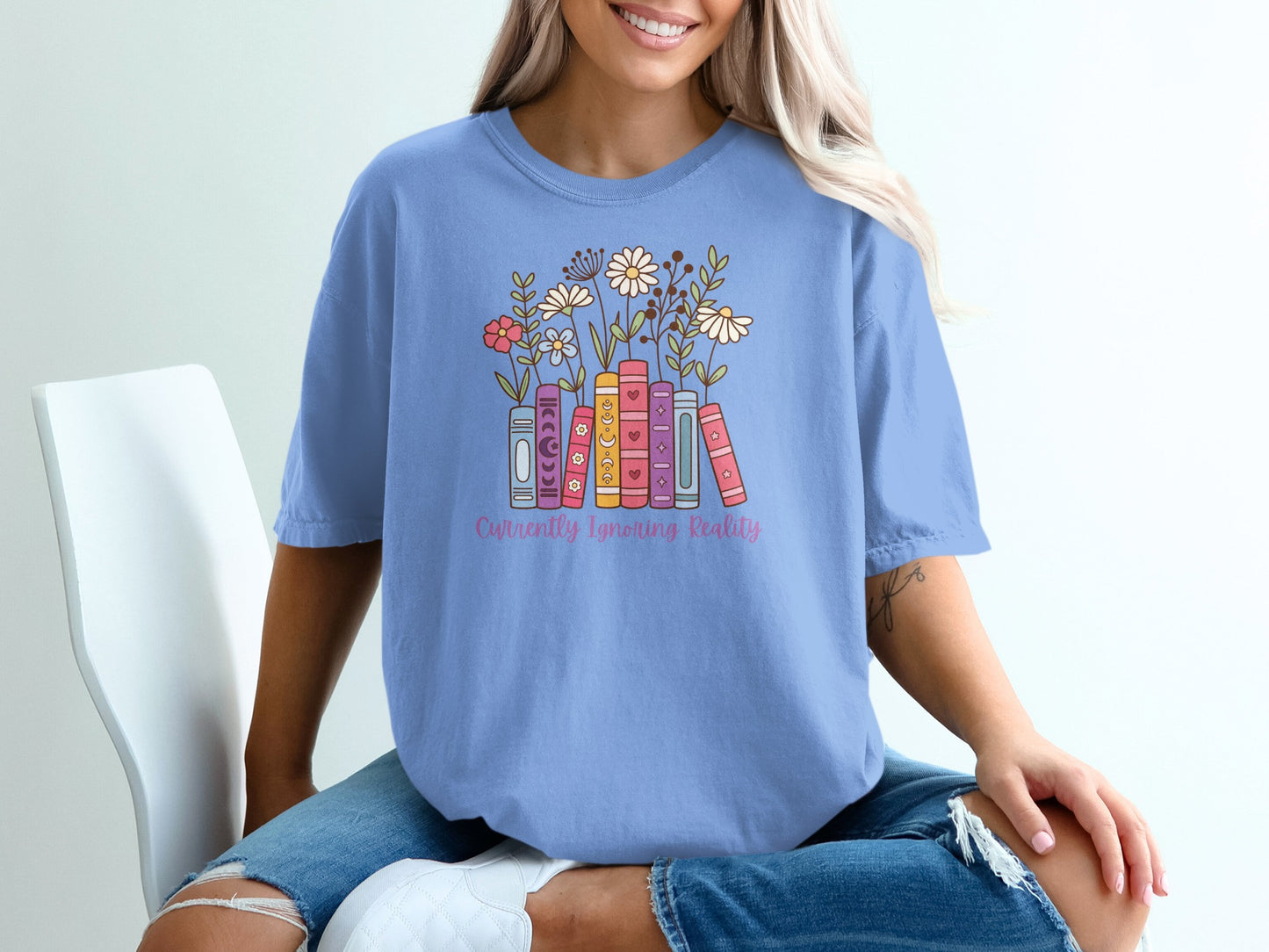 Light blue t-shirt with stacked books and flowers, reading "Currently Ignoring Reality".