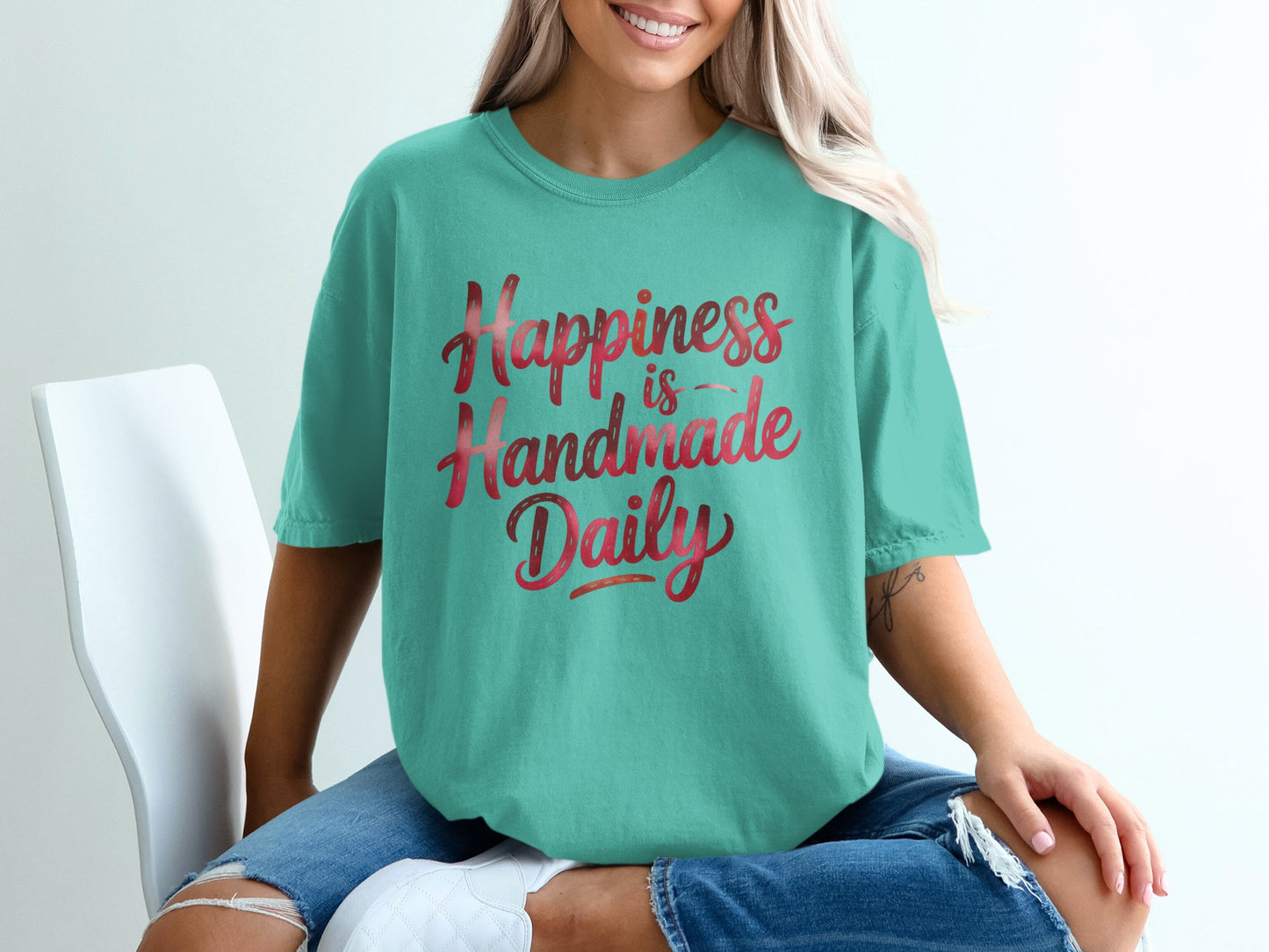 Teal t-shirt with "Happiness is Handmade Daily" text in pink watercolor.