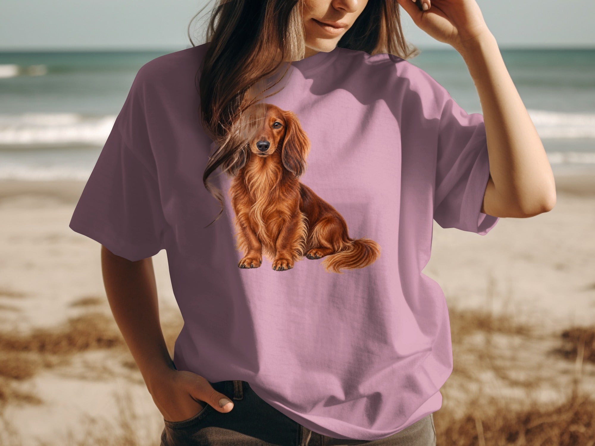 Long-haired red dachshund illustration on a pink t-shirt worn by a person at the beach.