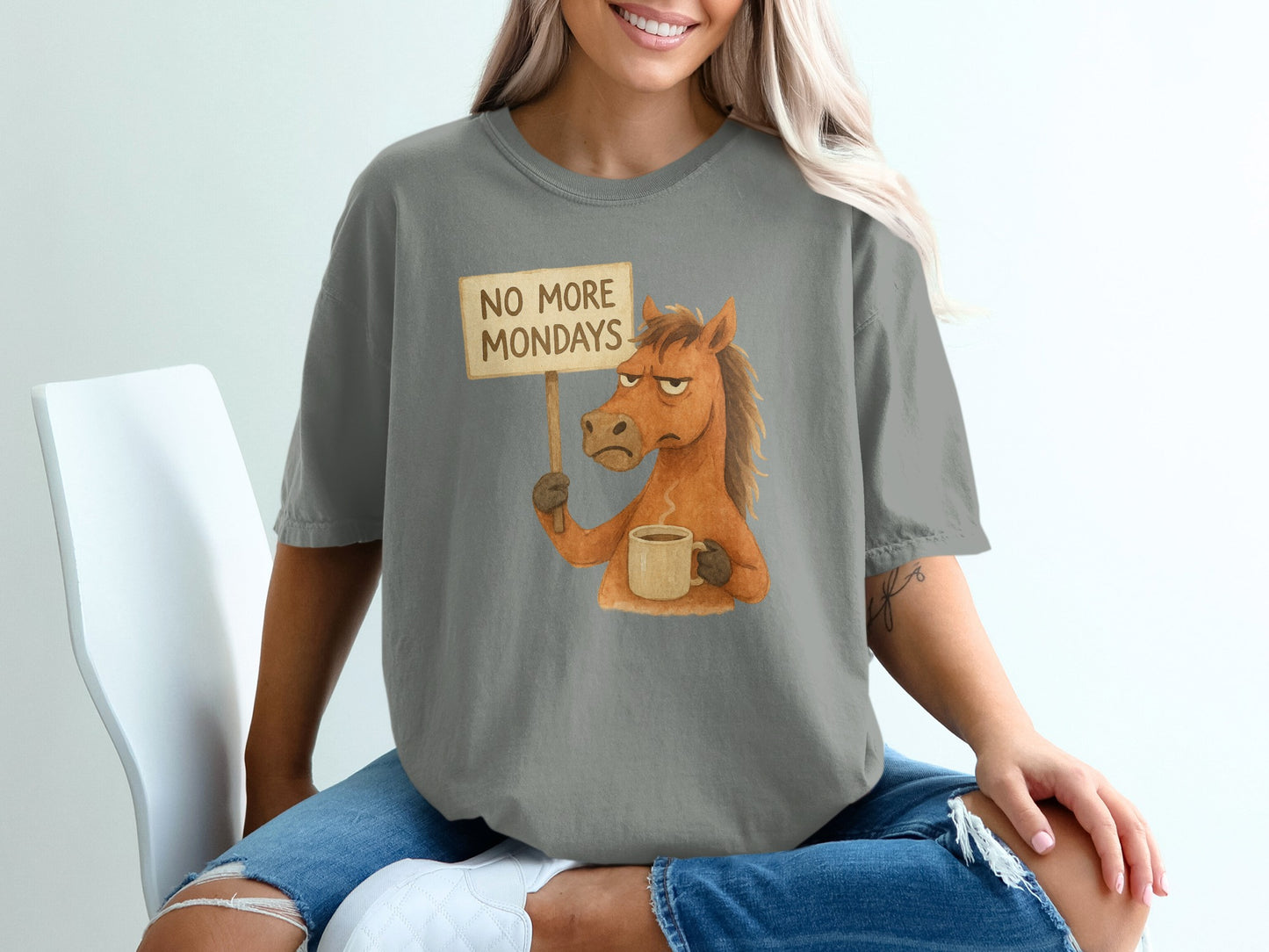 Horse holding "No More Mondays" sign and coffee mug, cartoon graphic on grey t-shirt.