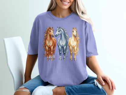 Three watercolor horses in tan, grey, and cream on a purple t-shirt.