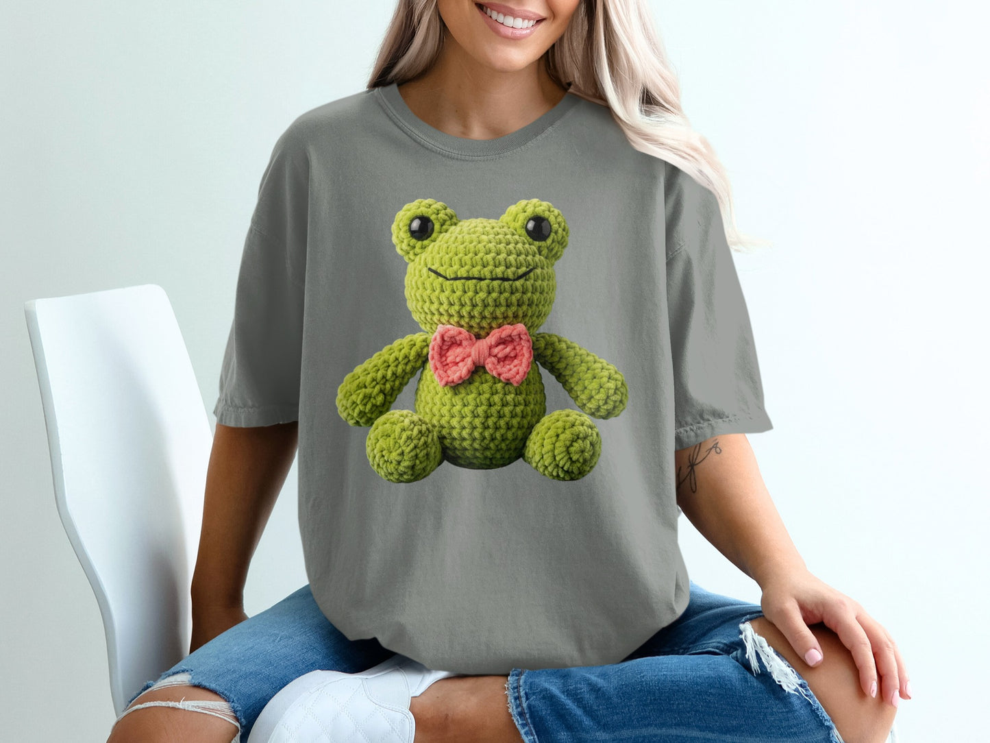 Crocheted frog with pink bow on a gray t-shirt.